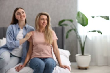 Evdeki yatakta oturan mutlu genç kadınların bulanık görüntüsü, mesaj için yer.