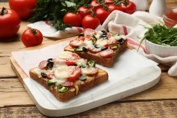 Tasty pizza toasts, arugula and tomatoes on wooden table