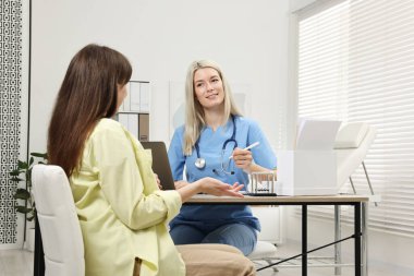 Gülümseyen doktor klinikteki hamile hastaya danışıyor.