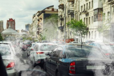 Çevre kirliliği. Şehirdeki hava dumanla kirlenmiş. Yoldaki egzozlarla çevrili arabalar.