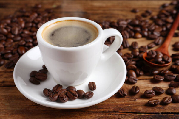Steaming coffee in cup and roasted beans on wooden table