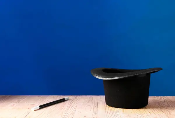 蓝色背景的木制桌子上的魔术师帽和魔杖 文字空间 图库图片