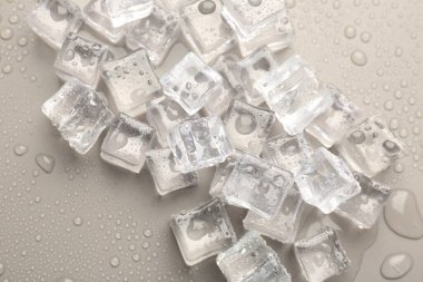 Eriyen buz küpleri ve açık gri arkaplanda su damlaları.