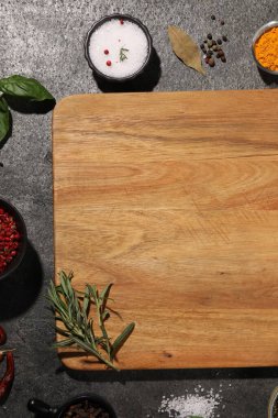 Gri desenli masa üzerindeki baharatlarla çevrili ahşap kesme tahtası. Metin için boşluk