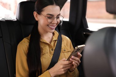 Emniyet kemeri takmış bir kadın arabanın içinde telefon kullanıyor.