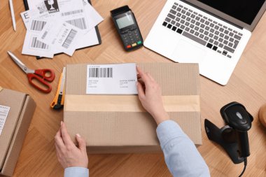 Paketleme. Postane çalışanı, ahşap masadaki kutuya barkod yapıştırıyor.