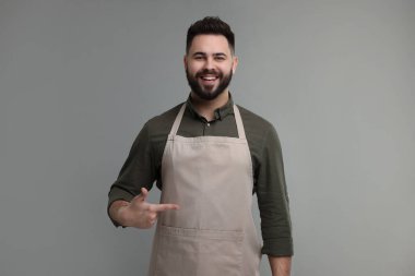 Gülümseyen adam gri arka plandaki mutfak önlüğünü işaret ediyor. Tasarım için model