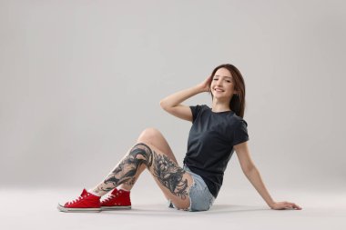 Gülümseyen dövmeli kadın gri arka planda poz veriyor.