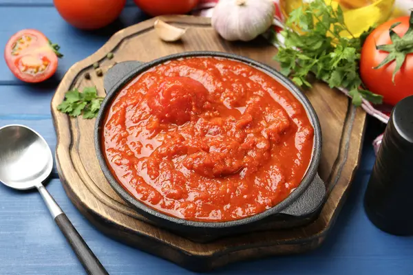 Ev yapımı domates sosu kasede, kaşık ve malzemeler mavi ahşap masada.