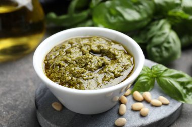 Lezzetli pesto sosu kasede, fesleğen ve çam fıstığı gri masada, yakın plan