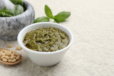 Lezzetli pesto sosu kasede, fesleğende, çam fıstığında ve kaşıkta açık gri masada, mesaj için yer var.