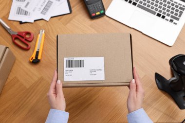 Postane çalışanı ahşap masada paket paketliyor.