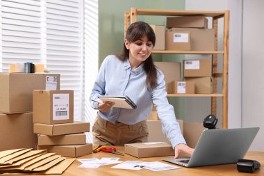 Paketleme. Kapalı alandaki ahşap masada dizüstü bilgisayar kullanan postane çalışanı.