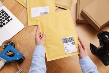Postane çalışanı ahşap masada paket paketliyor.