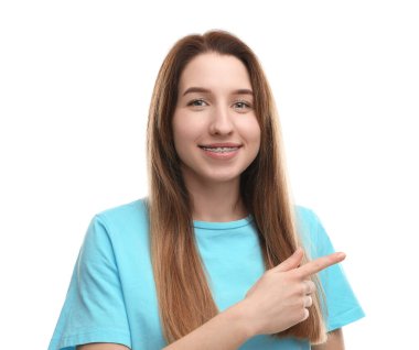 Dişlerinde diş teli olan gülümseyen bir kadının portresi beyaz arka planda bir şeyi işaret ediyor.