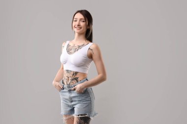 Gri arkaplanda gülümseyen dövmeli kadın portresi