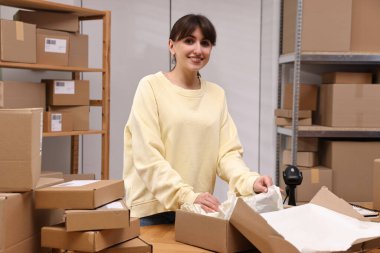 Postane çalışanı içeride ahşap masada paket paketliyor.