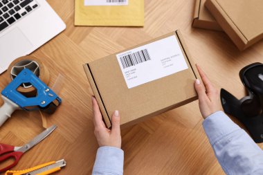 Postane çalışanı ahşap masada paket paketliyor.