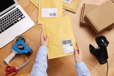 Postane çalışanı ahşap masada paket paketliyor.