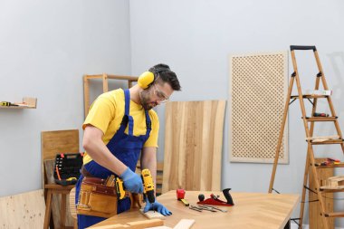 Genç işçi atölyedeki masada elektrikli matkap kullanıyor.