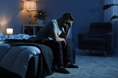 Hüsrana uğramış bir adam gece yatakta oturuyor.
