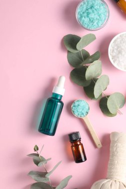 Pembe arka planda farklı aromaterapi ürünleri ve okaliptüs dalları.