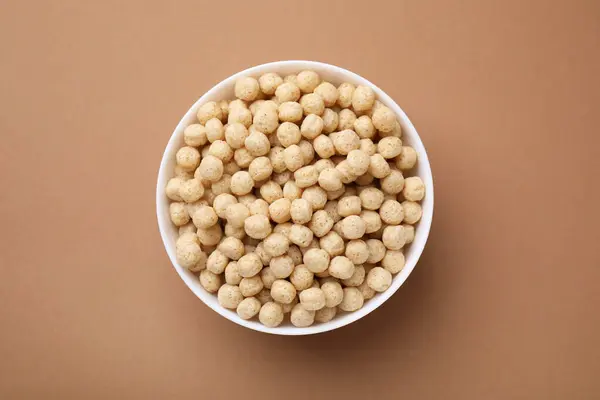 stock image Tasty cereal balls in bowl on brown table, top view