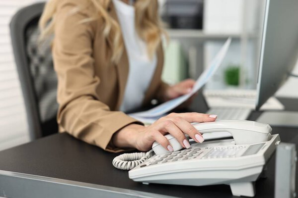 Secretary dialing number on telephone at table in office, closeup