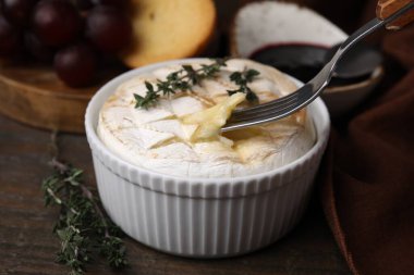 Ahşap masadaki çatalla lezzetli pişmiş camembert yemek, yakın plan.