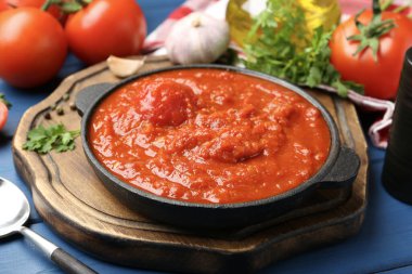 Ev yapımı domates sosu kasede ve malzemeler mavi masada, yakın plan.