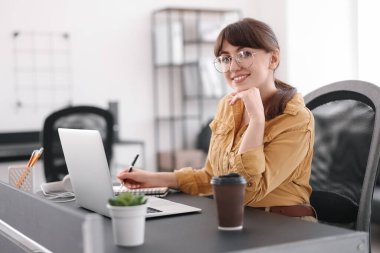 Woman taking notes during webinar at table indoors