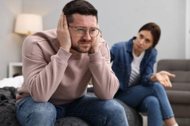 Stressed husband ignoring his wife in bedroom, selective focus. Relationship problems
