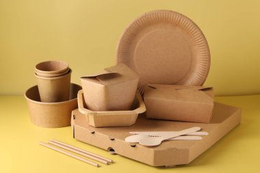 Çevre dostu gıda ambalajı. Soluk sarı arkaplanda kağıt kaplar ve sofra takımı