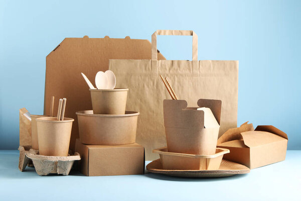 Eco friendly food packaging. Paper containers, tableware and bag on white table against light blue background