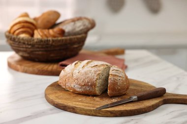 Hasır ekmek sepeti, taze fırınlanmış somunlar ve mutfaktaki beyaz mermer masada bıçak.
