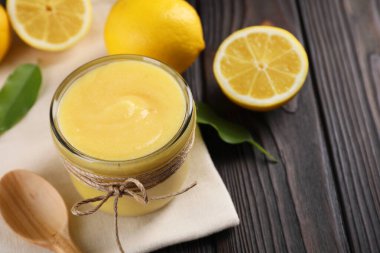 Cam kavanozda lezzetli limon ezmesi, taze narenciye meyvesi, yeşil yapraklar ve ahşap masada kaşık, yakın plan.