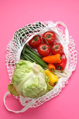 Parlak pembe arka planda farklı sebzeler bulunan ip torbası, üst manzara.