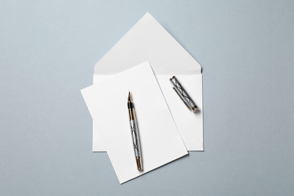 Blank sheet of paper, letter envelope and pen on grey background, top view