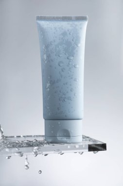 Cam üzerinde nemlendirici krem ve gri arka planda su damlaları.