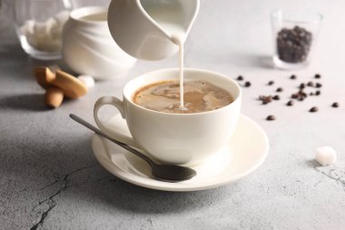 Sütü bardağa doldururken açık gri desenli masa, yakın çekim.