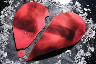 Halves of torn paper heart and ash on dark background