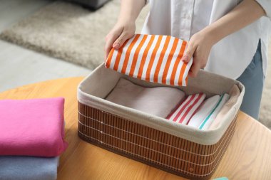 Kadın, katlanmış giysileri kapalı bir masada depoya koyuyor.