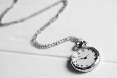 Beyaz ahşap masada zincirli gümüş cep saati, yakın plan.