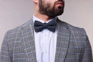Takım elbiseli, gömlekli ve papyonlu adam gri arka planda, yakın plan.