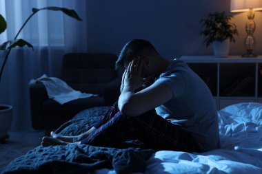 Tired man sitting on bed at night