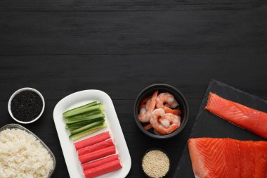Suşi yapıyorum. Siyah ahşap masa üzerinde malzemelerle bezenmiş düz bir kompozisyon. Metin için boşluk