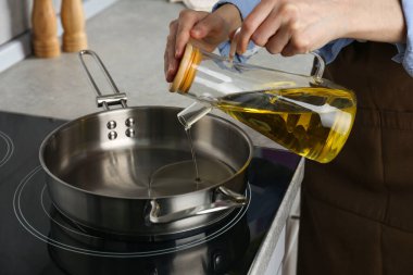 Vegetable fats. Woman pouring cooking oil into frying pan on stove in kitchen, closeup