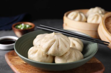 Lezzetli bao çörekleri (baozi) kasede ve çubuklar gri masada, yakın plan