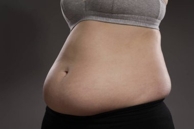 Gri arka planda aşırı göbek yağlı kadın, yakın plan. Aşırı kilolu