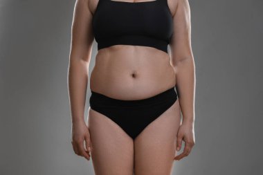 Gri arka planda aşırı göbek yağlı kadın, yakın plan. Aşırı kilolu